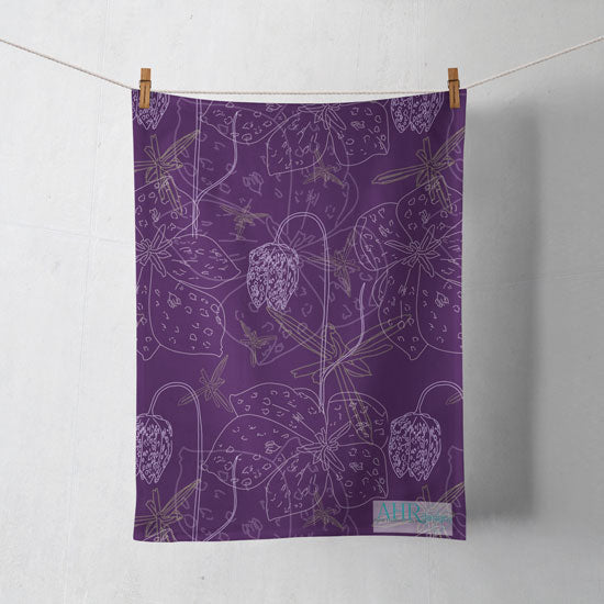 Colourful gift – Purple, White and Yellow Fritillaria flower design tea towel hanging from clothesline, shadows showing on off-white background. Designed by Anne Harrington Rees. Designed, printed and made in Ireland.