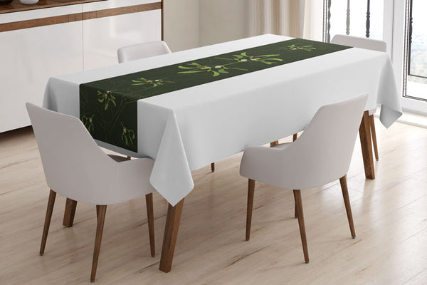 Mistletoe table runner designed by Anne Harrington Rees, viewed on a table covered with a white tablecloth.  Symmetrical design of leaves and berries on a dark green background.