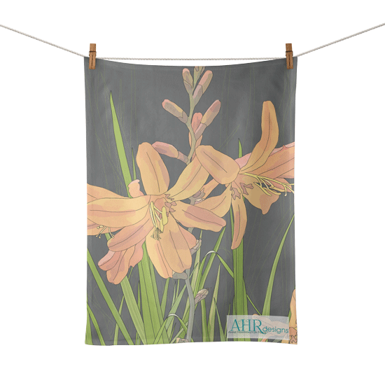 Colourful gift – Orange, Pink, Green and Grey Montbretia flower design tea towel hanging from clothesline, transparent background. Designed by Anne Harrington Rees. Designed, printed and made in Ireland.