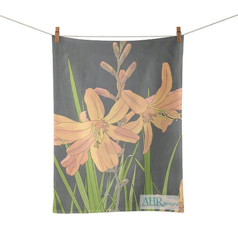 Colourful gift – Orange, Pink, Green and Grey Montbretia flower design tea towel hanging from clothesline, transparent background. Designed by Anne Harrington Rees. Designed, printed and made in Ireland.
